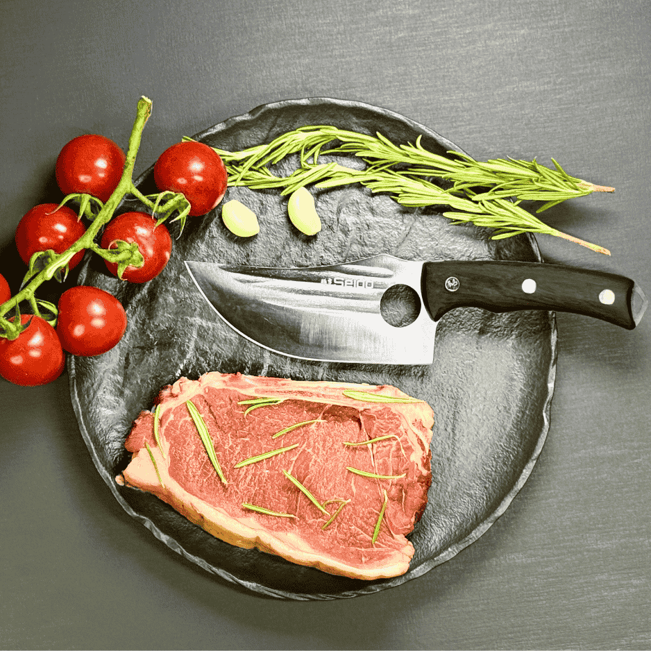Vachelli Akamori stainless steel butcher knife on plate with raw steak, rosemary, garlic, and tomatoes.
