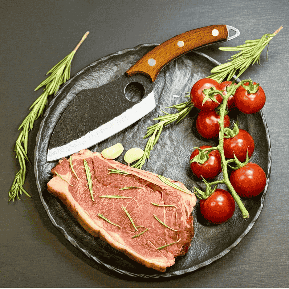 Vachelli Marova forged carbon steel cleaver displayed with raw steak, rosemary, garlic, and tomatoes.