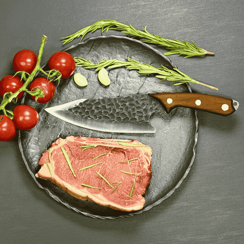 Vachelli Zanari forged carbon steel chef knife displayed with raw steak, rosemary, garlic, and tomatoes.